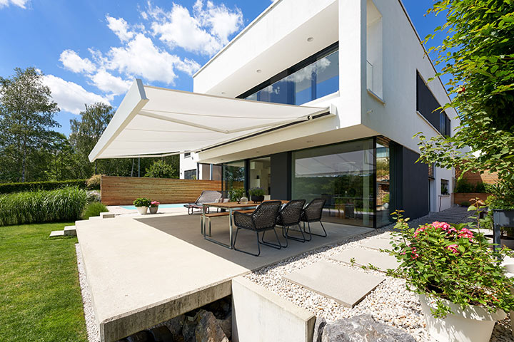 Modern house with a terrace, featuring a large awning and outdoor dining area surrounded by greenery.