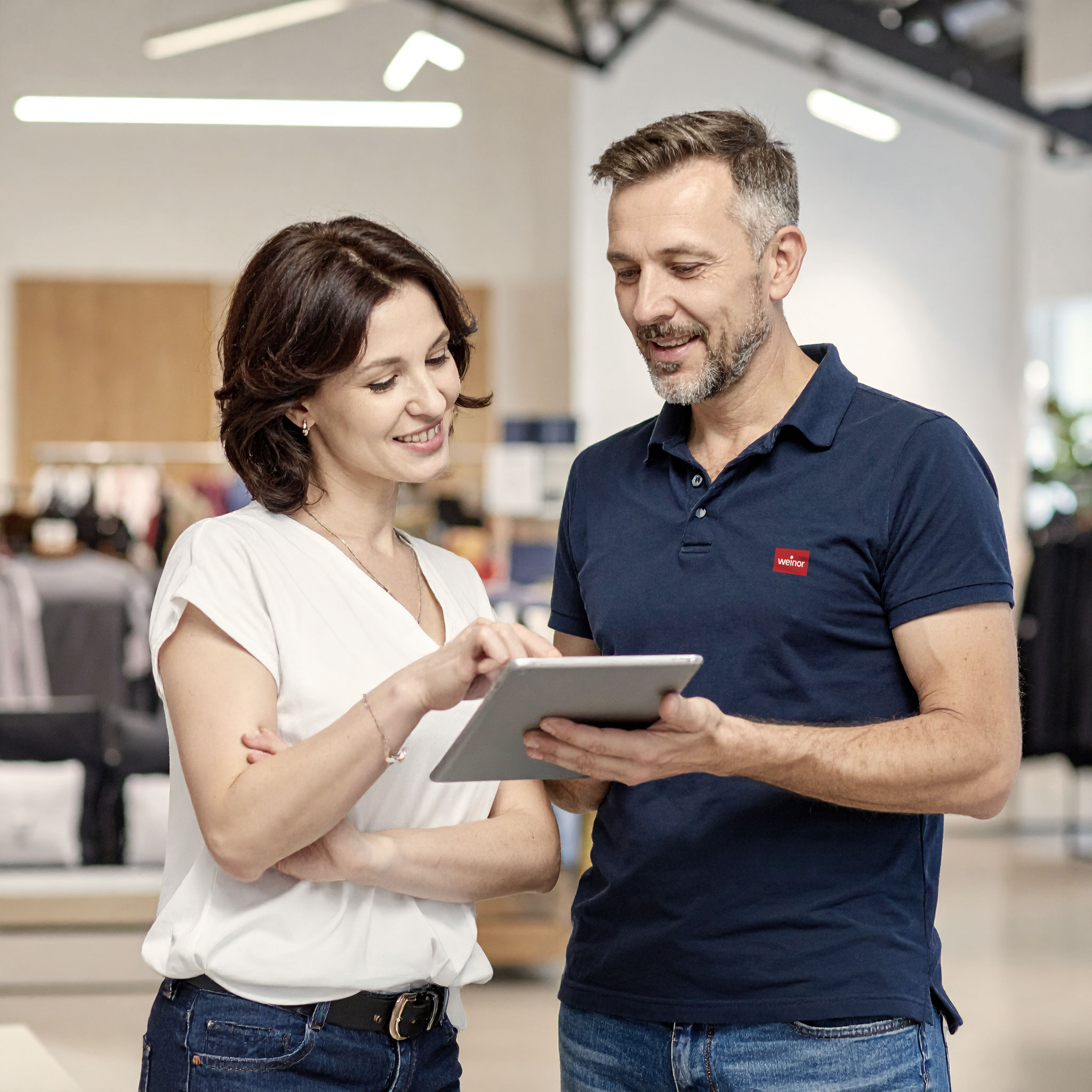 Eine Frau und ein Mann betrachten gemeinsam ein Tablet in einem Verkaufsraum.