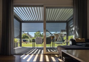 Ein lichtdurchfluteter Wintergarten mit horizontalen Lamellen und Blick auf eine grüne Terrassensituation.