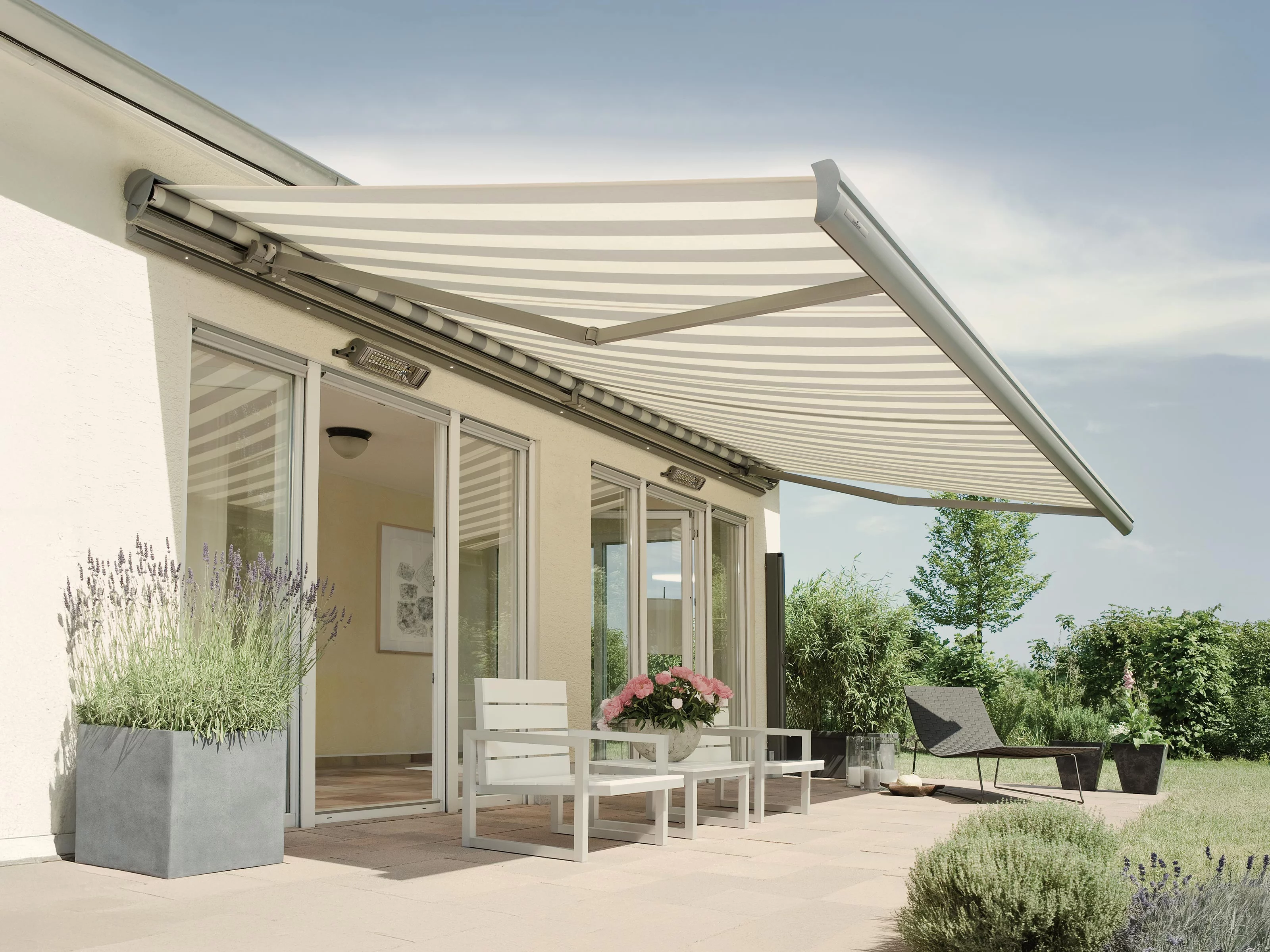 A terrace with a striped awning, modern furniture, and greenery in a sunny outdoor setting.
