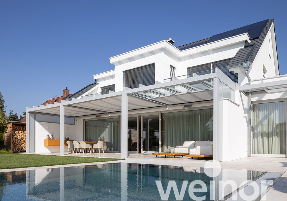 Modernes Haus mit Überdachung, großem Glasfenster und Pool in einer grünen Umgebung. 