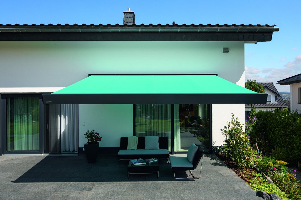 Green awning extended over a terrace area with seating and lush greenery in the background.