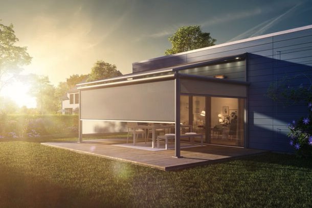 Moderne overkapping met een gesloten zonweringdoek in een groene tuin bij zonsondergang.