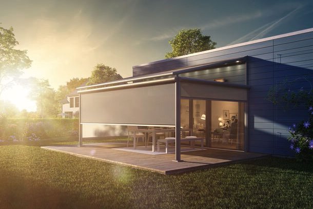 A modern home extension with a glass facade and an outdoor area, set against a sunset.