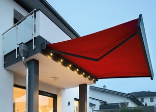 Rood zonweringdoek met verlichting, gemonteerd aan een moderne woning. 