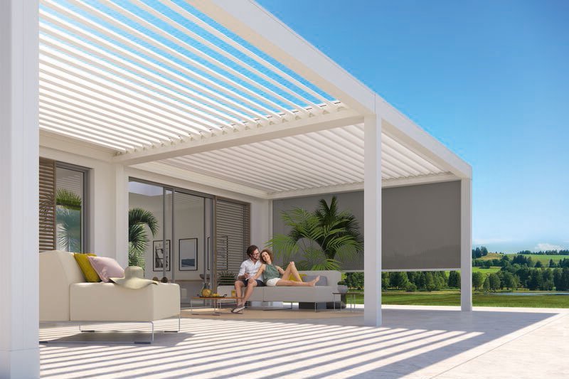 Terrassensituatie onder een moderne overkapping met schaduwdoeken en uitzicht op groene velden.