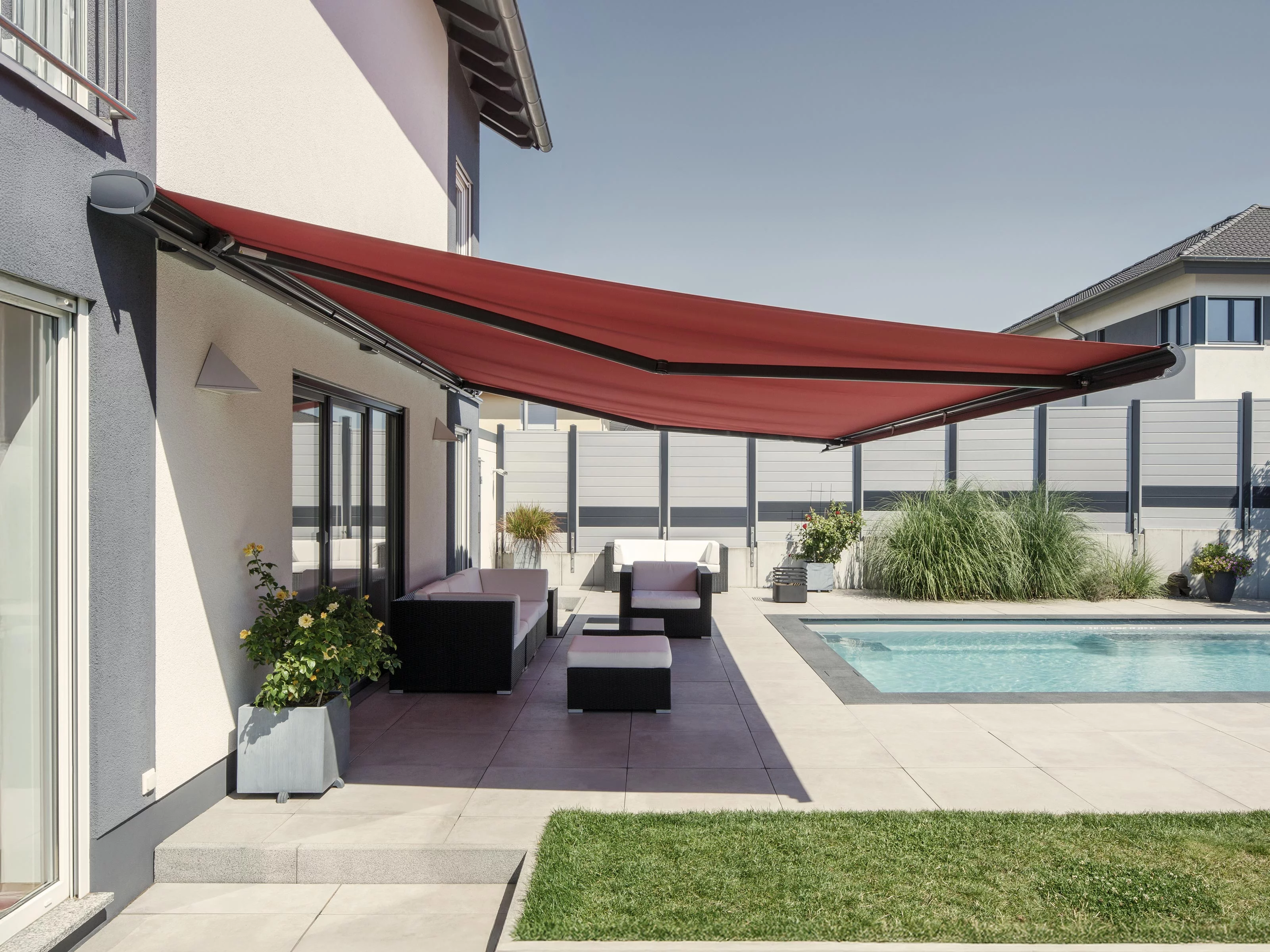Terrassensituation avec une markise rouge et une piscine, entourée de verdure et de pavés.