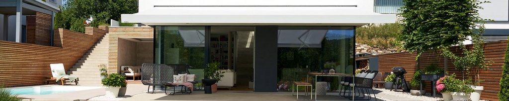Moderne Terrasse mit Glasfront, Überdachung und Terrassensituation, umgeben von Pflanzen und Holzstrukturen. Moderne Terrasse mit Glasfront, Überdachung und Terrassensituation, umgeben von Pflanzen und Holzstrukturen.