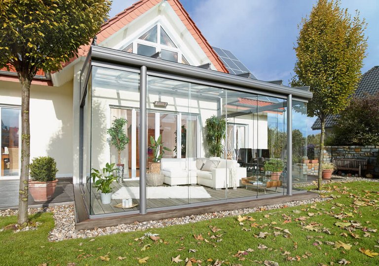 Terrassensituation mit Glas-Schiebewänden, Überdachung und Pflanzen im Außenbereich.