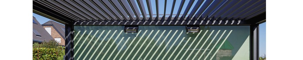 Shadows created by a slatted structure over a glass wall, with a blue sky visible above.