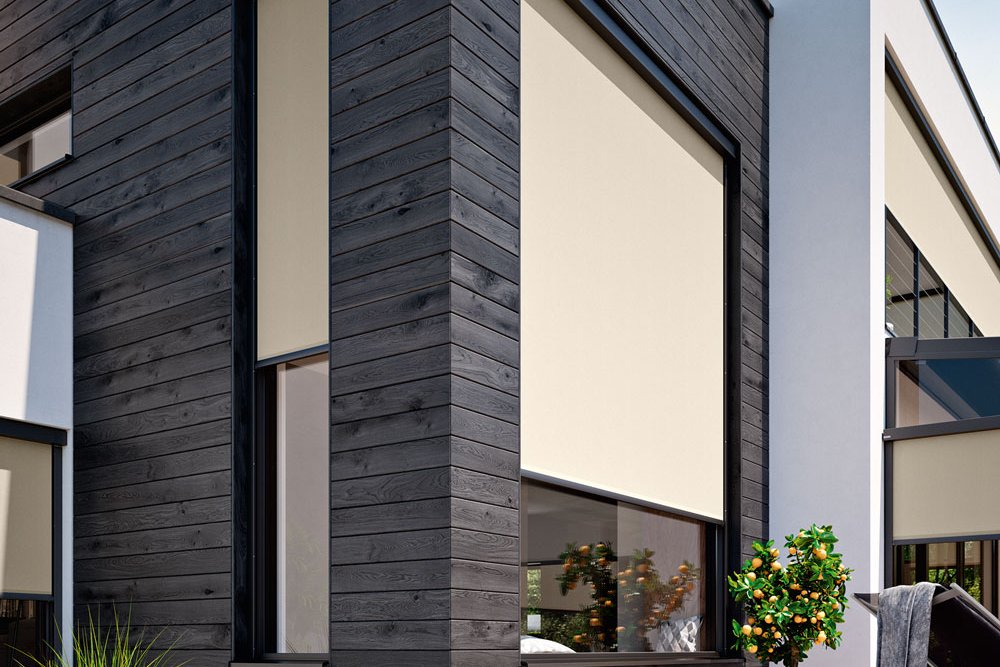 Moderne woning met zwarte gevel, grote ramen en beige zonneschermn aan de gevel. Terrassensituatie met planten.