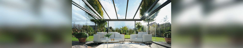 Moderne Terrassensituation mit Glas-Schiebewänden und eleganten Möbeln unter einem transparenten Dach.