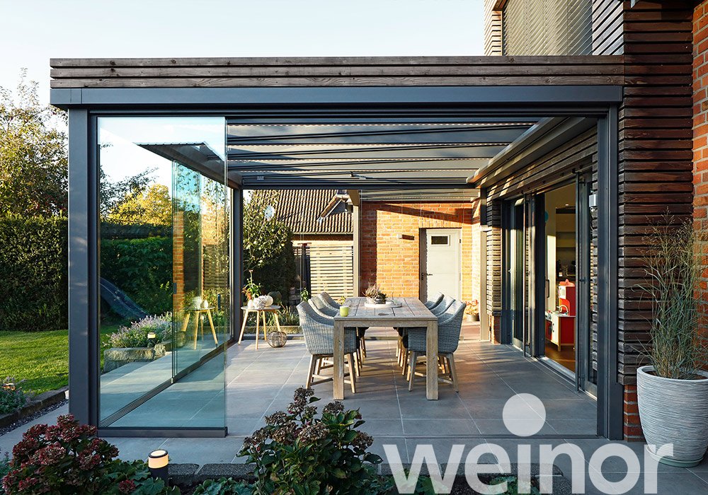 Moderne Überdachung mit Glas-Schiebewänden und Terrassensituation in einem hellen, einladenden Ambiente. 