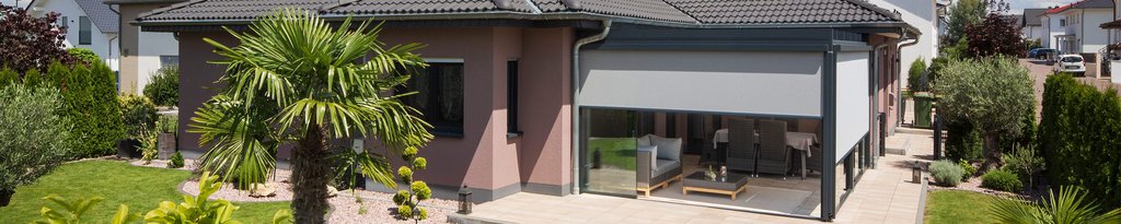 Ein modernes Haus mit einer Überdachung, umgeben von grüner Terrassensituation und Gartenanlagen.