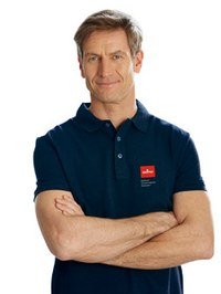 Mann mit verschränkten Armen in dunkelblauer Poloshirt, freundlicher Gesichtsausdruck.