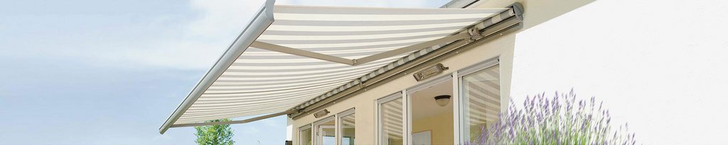 Markise mit gestreiftem Markisentuch über einer Terrassensituation, im Hintergrund ein heller Hausanbau.