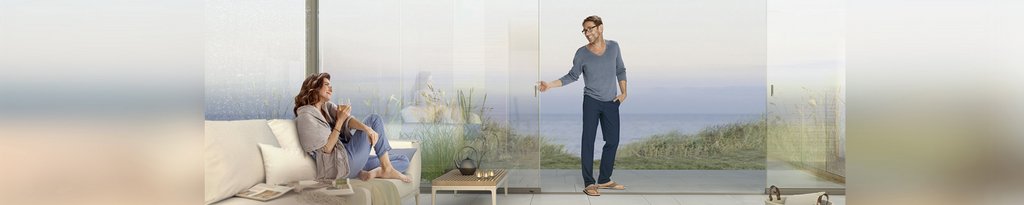 Zwei Personen in einer modernen Terrassensituation mit Glas-Schiebewänden und Ausblick auf das Meer.