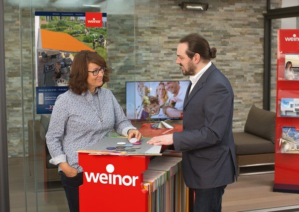 Deux personnes discutent autour d'une table, dans un espace moderne avec des brochures et un écran.