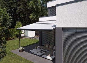 Moderne woning met een overkapping, terras en groen grasveld. De kleuren zijn voornamelijk grijs en wit. 