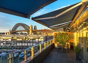 Terras met zonneschermn, uitzicht op een brug en moderne architectuur in een havengebied. 