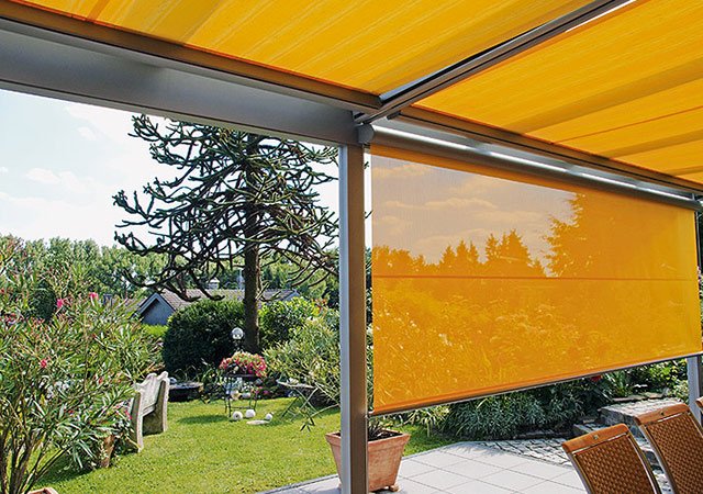 Sonnenschutz in Gelb mit Markisenkasten, Blick auf eine grüne Gartenlandschaft.